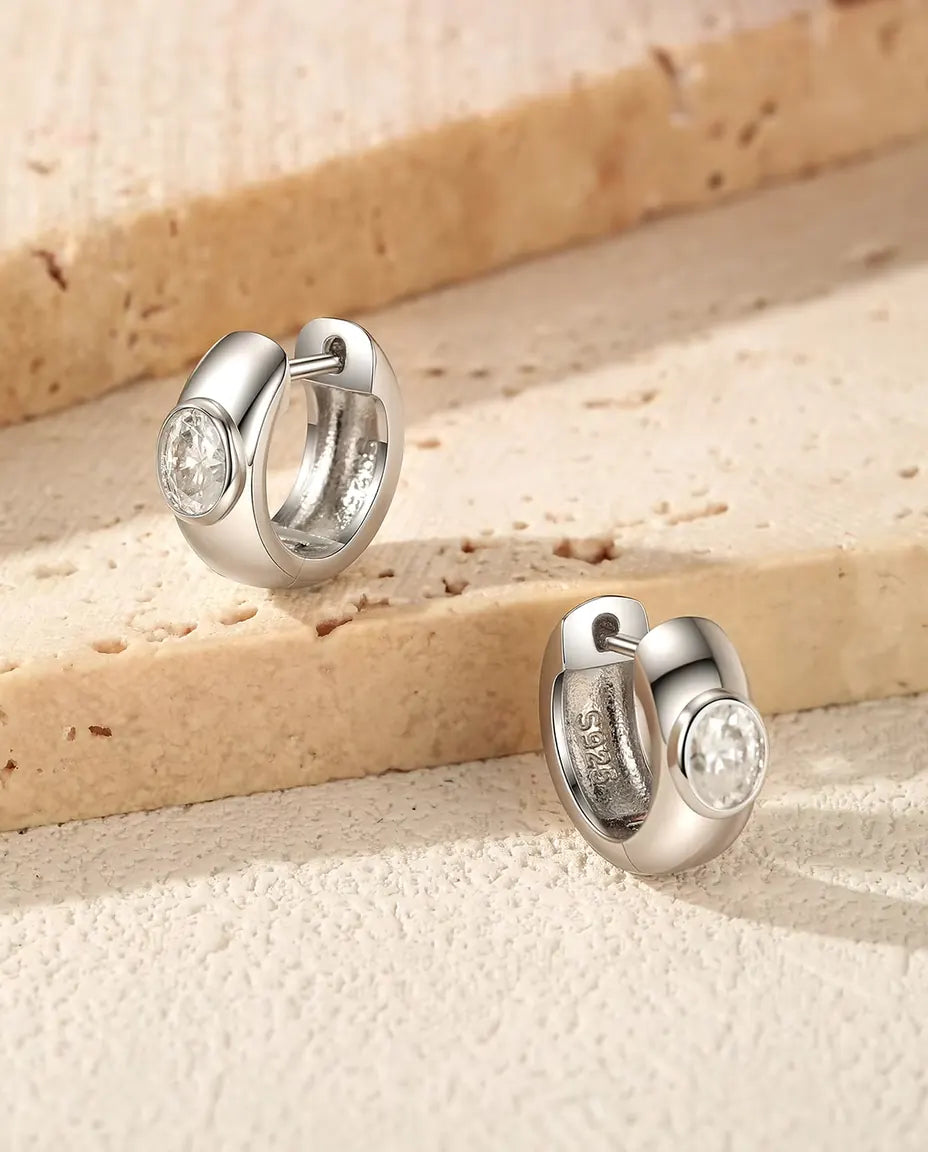 Breda Små Creoler med Oval Moissanit i 925 Sterlingsilver - paret på trappsteg av travertin