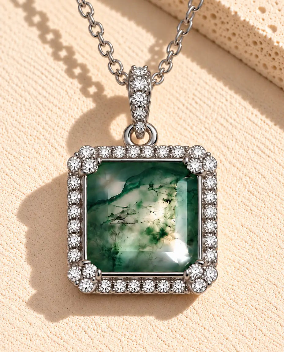 Moss Agate Halsband med Fyrkantig Sten i 925 Sterlingsilver - liggande på en ljus strukturerad yta bredvid ett travertinblock