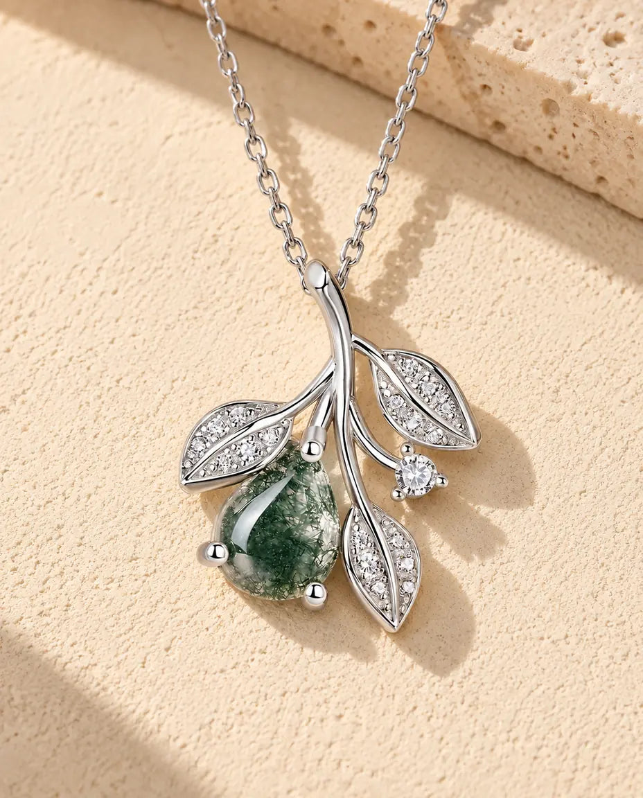 Moss Agate Halsband med Blad i 925 Sterlingsilver - liggande på en ljus strukturerad yta bredvid ett travertinblock