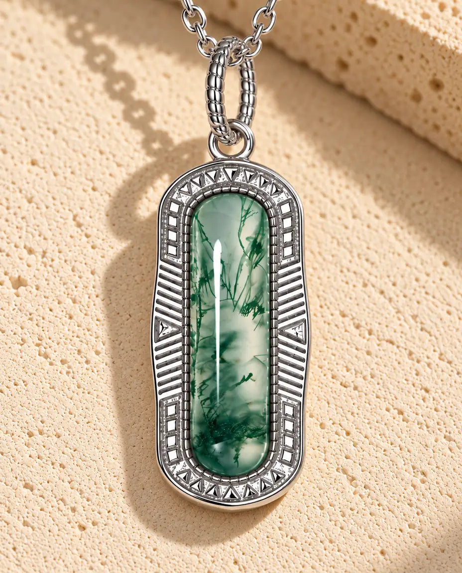 Moss Agate Halsband med Kapselhänge i 925 Sterlingsilver - liggande på en ljus strukturerad yta bredvid ett travertinblock