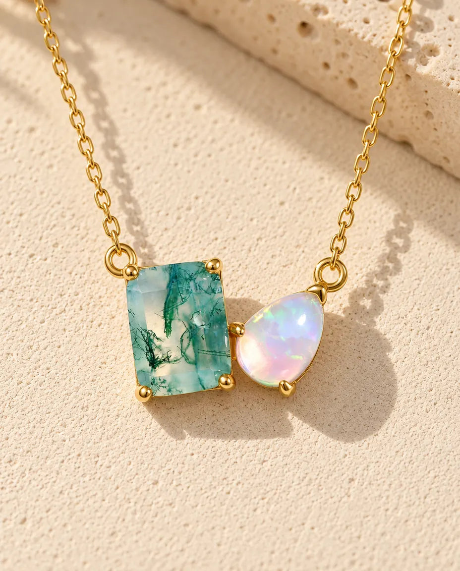 Moss Agate och Opal Halsband i Guldpläterat 925 Sterlingsilver - liggande på en ljus strukturerad yta bredvid ett travertinblock