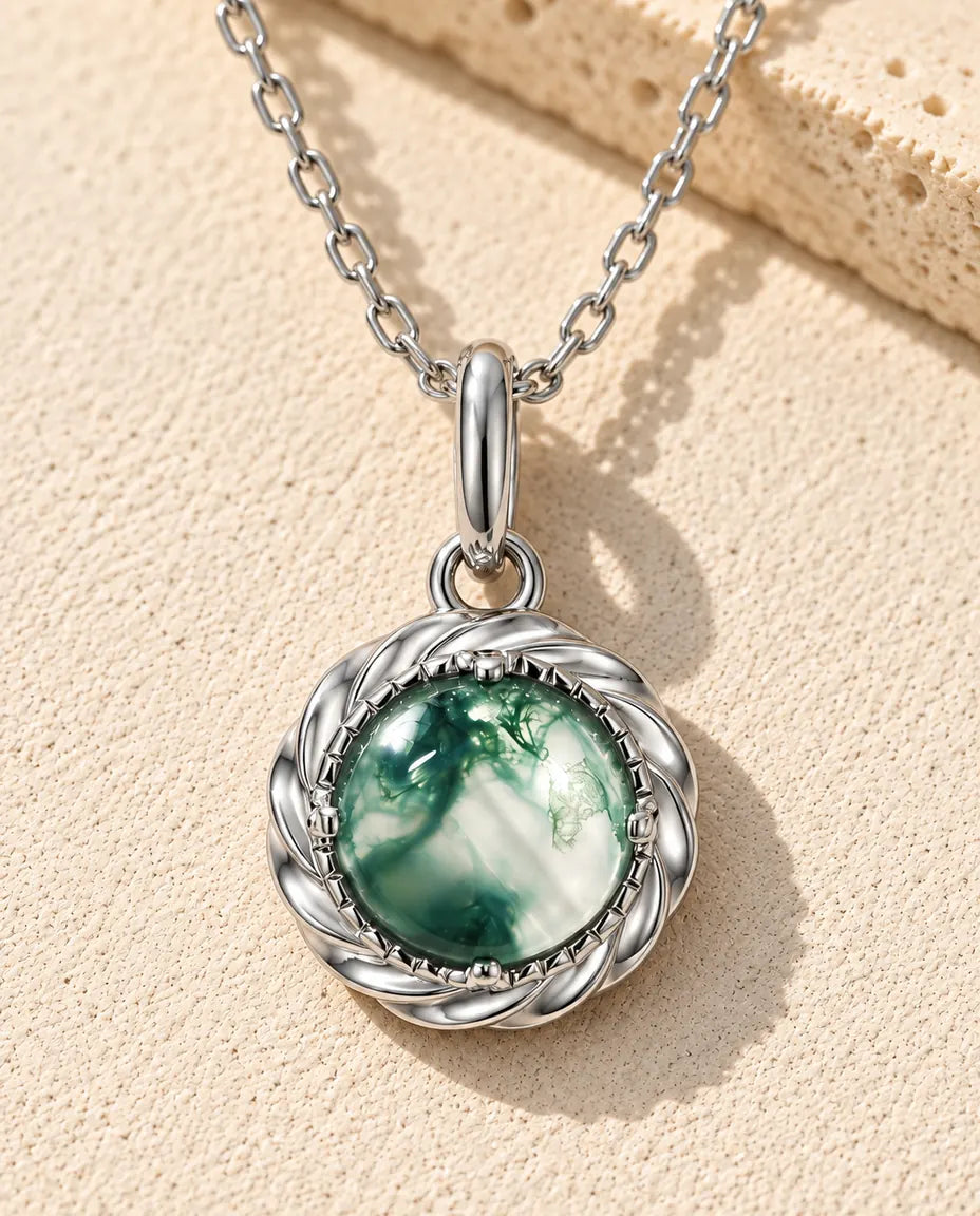 Rund Moss Agate Halsband med Hänge i 925 Sterlingsilver - liggande på en ljus strukturerad yta bredvid ett travertinblock