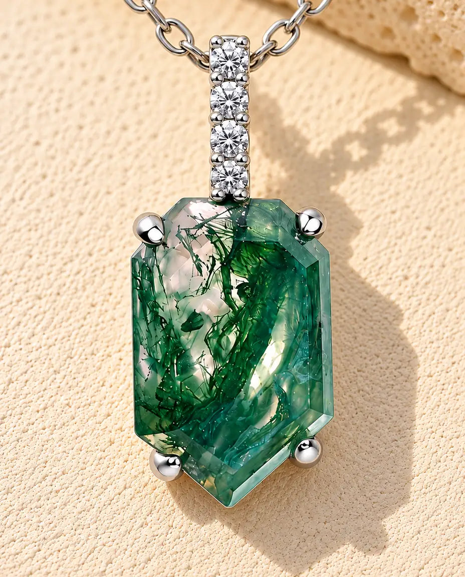 Moss Agate Halsband med Sköldformat Hänge i 925 Sterlingsilver - liggande på en ljus strukturerad yta bredvid ett travertinblock