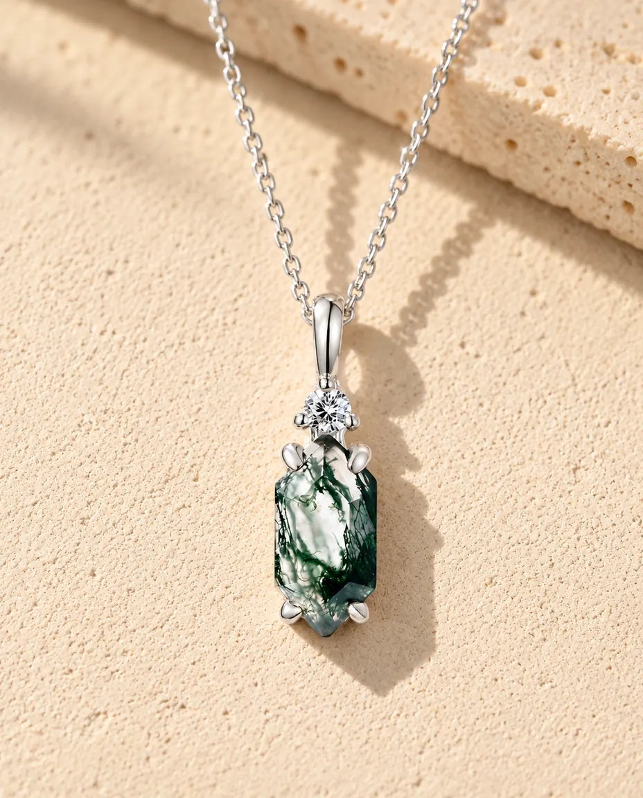 Moss Agate Halsband med Smal Hexagon i 925 Sterlingsilver - liggande på en ljus strukturerad yta bredvid ett travertinblock
