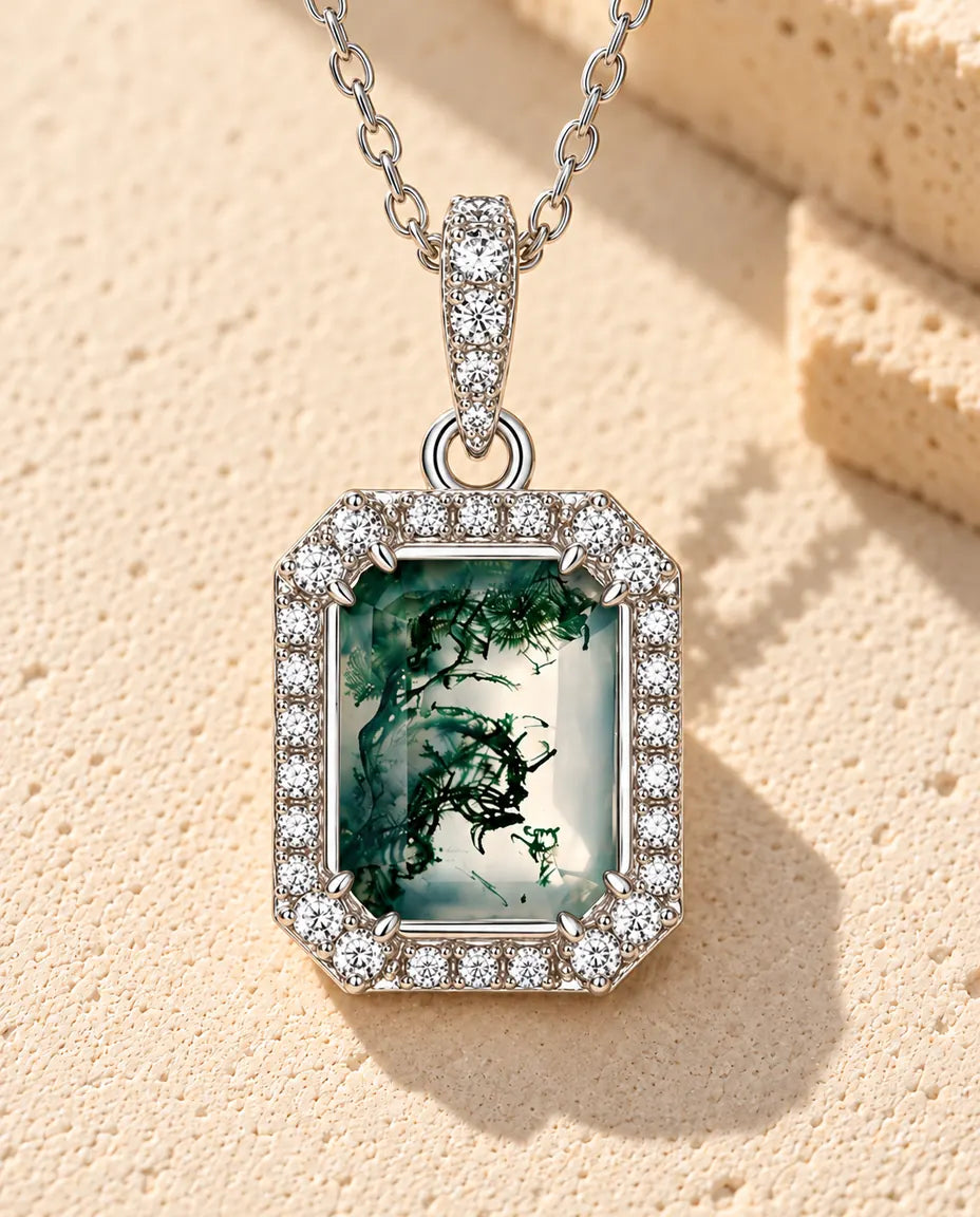 Moss Agate Halsband med Smaragdslipad Sten i 925 Sterlingsilver - liggande på en ljus strukturerad yta bredvid ett travertinblock