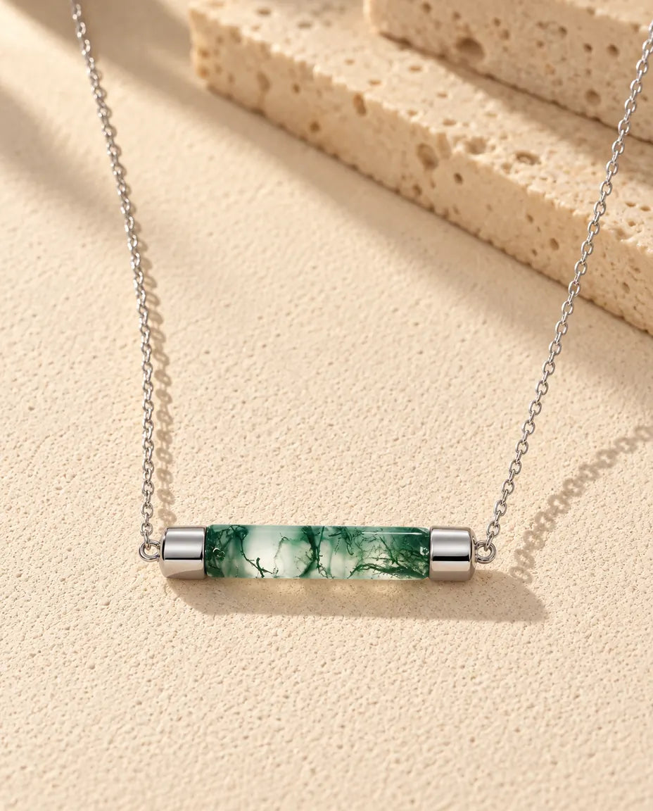 Moss Agate Halsband med Stav i 925 Sterlingsilver - liggande på en ljus strukturerad yta bredvid ett travertinblock