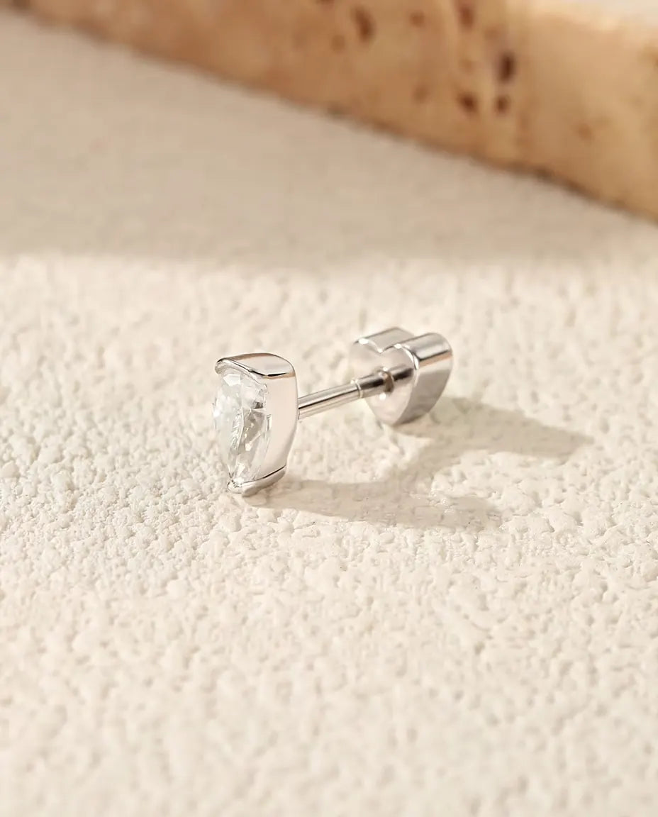 Stiftörhängen med Droppslipad Moissanit i 925 Sterlingsilver - på en ljus strukturerad yta bredvid en travertinplatta