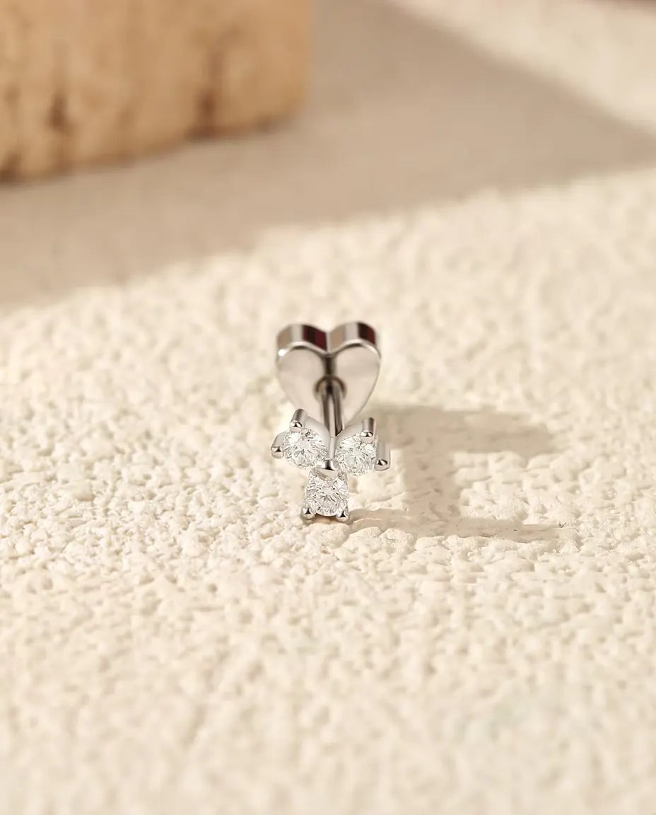 Stiftörhängen med Moissanit i Klöverform i 925 Sterlingsilver - stående på det hjärtformade låset, på en ljus strukturerad yta