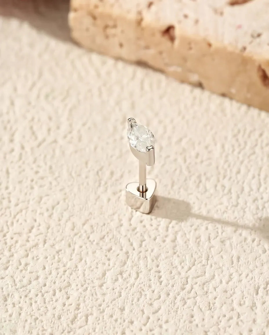 Stiftörhängen med Markisslipad Moissanit i 925 Sterlingsilver - stående på det hjärtformade låset, på en ljus strukturerad yta