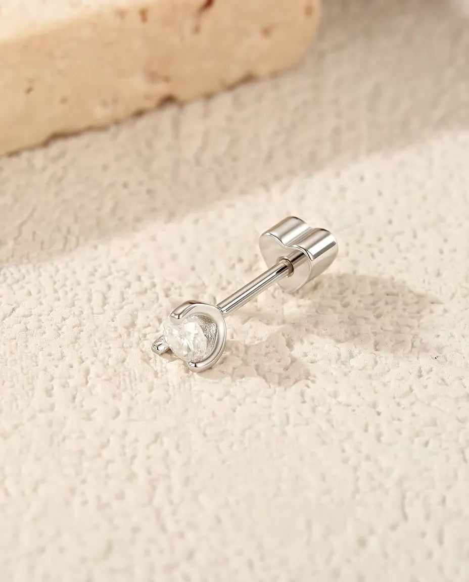 Stiftörhängen med Rund Moissanit och Silverbåge i 925 Sterlingsilver - liggande på sidan på en ljus strukturerad yta, hjärtformat lås på stiftet