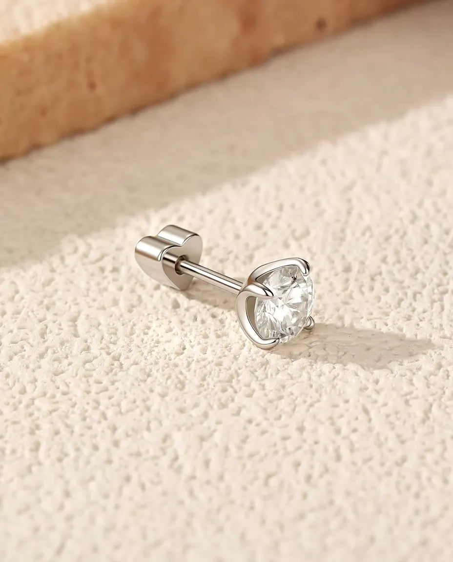 Stiftörhängen med Moissanitsolitär på 5 mm i Fyra Klor i 925 Sterlingsilver - liggande på sidan på en ljus strukturerad yta, hjärtformat lås på stiftet