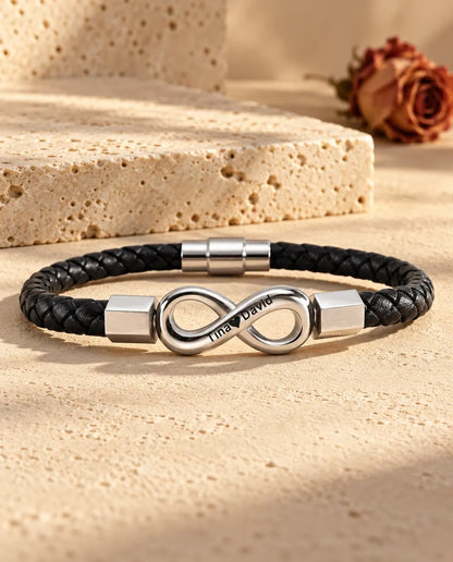 Silverfärgad oändlighetssymbol i rostfritt stål med sexkantiga ändhylsor på ett svart armband i flätat konstläder