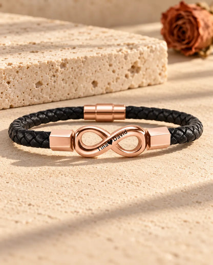 Roséguldfärgad graverad oändlighetssymbol på ett svart armband i flätat konstläder