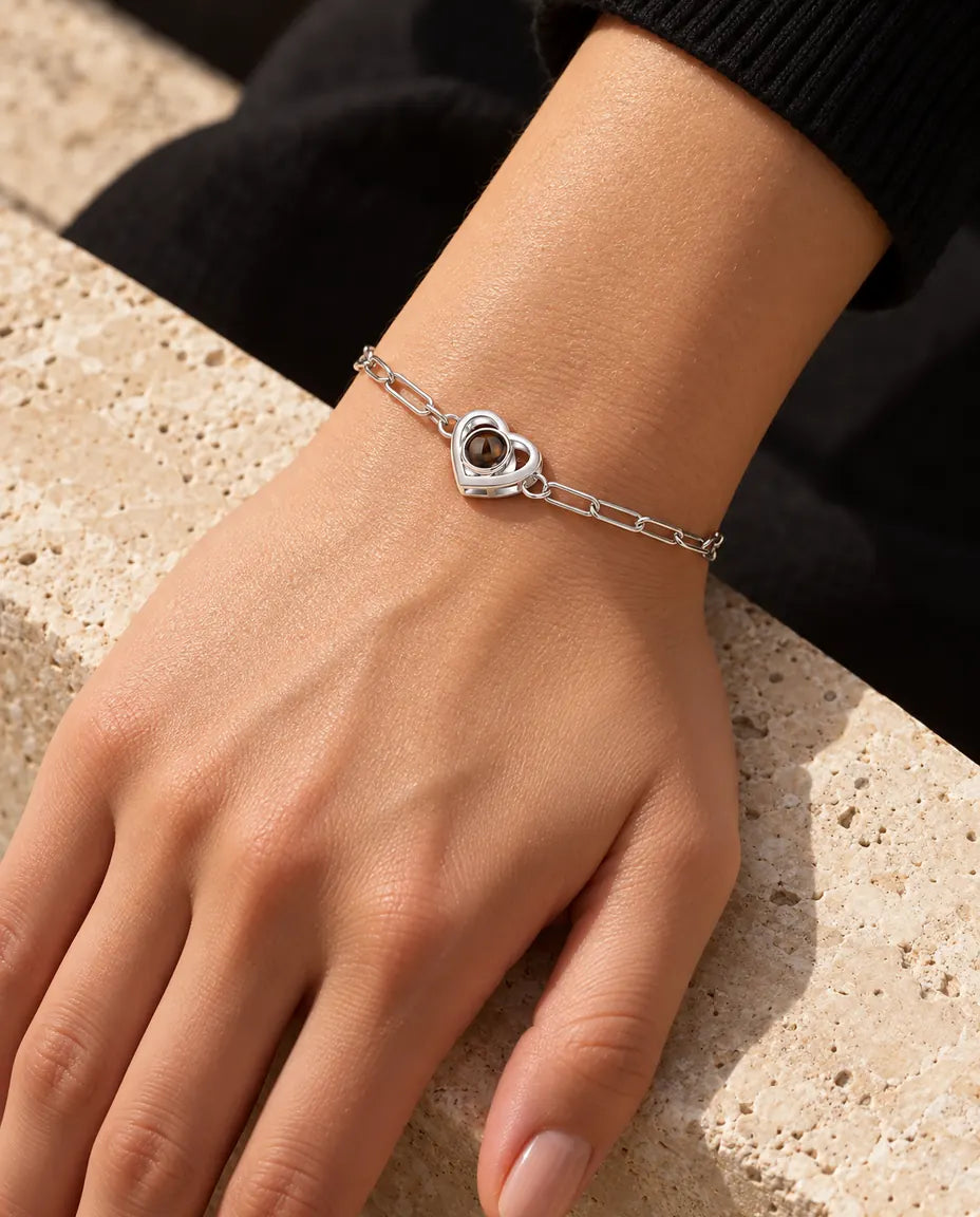 Kvinna bär det silverfärgade armbandet med dubbel hjärtberlock om handleden i varmt solljus