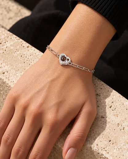 Kvinna bär det silverfärgade armbandet med dubbel hjärtberlock om handleden i varmt solljus