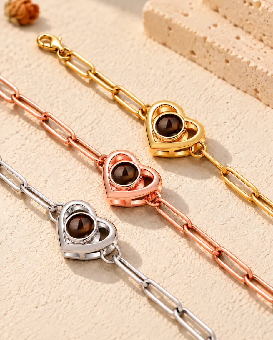 Närbild på ett guldfärgat, ett roséguldfärgat och ett silverfärgat armband med dubbelt hjärta