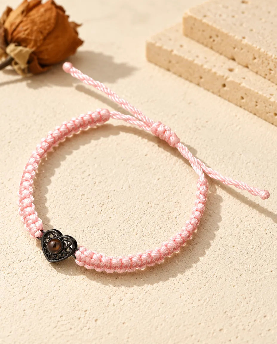 Armband med rosa flätad snodd och svart hjärtberlock som håller en brun projektionssten