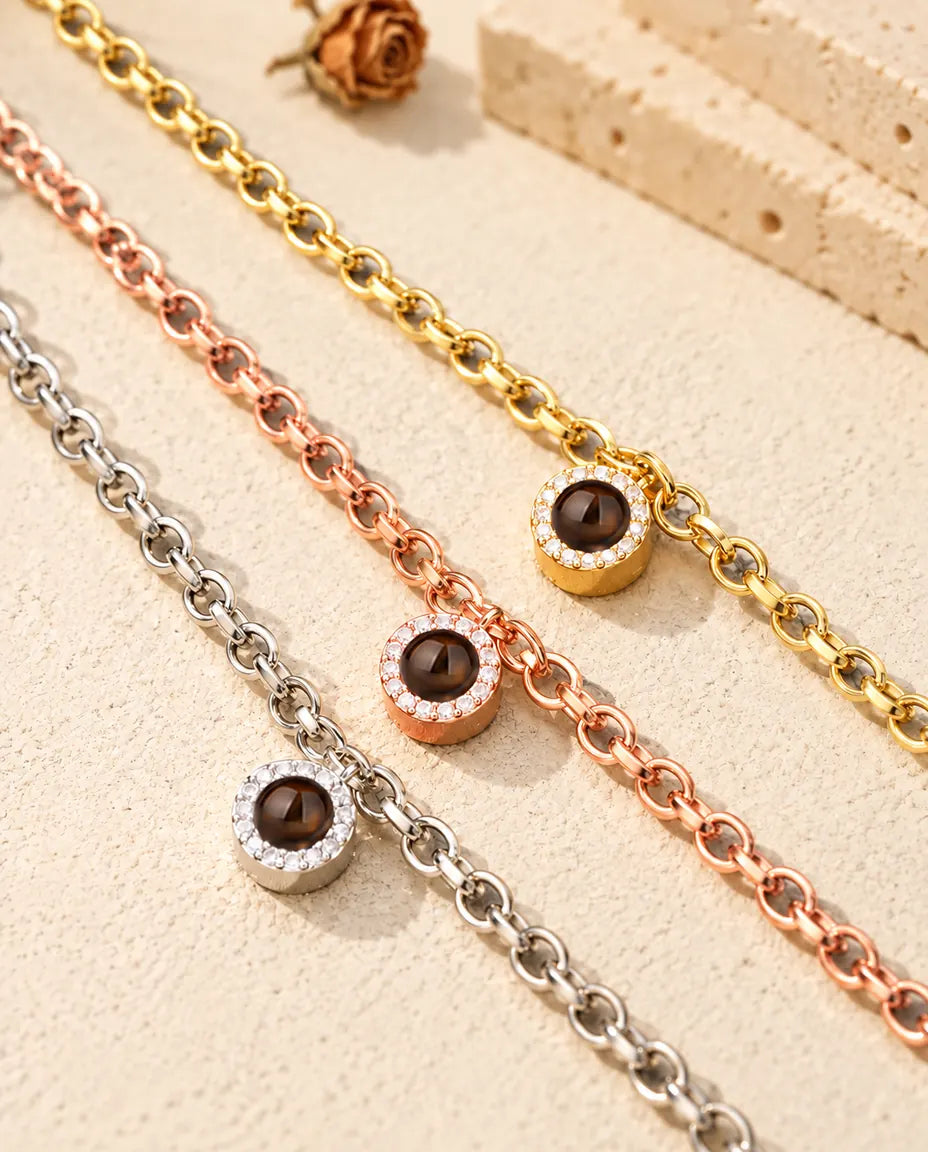 Närbild på ett guldfärgat, ett roséguldfärgat och ett silverfärgat armband med rund zirkoniaberlock