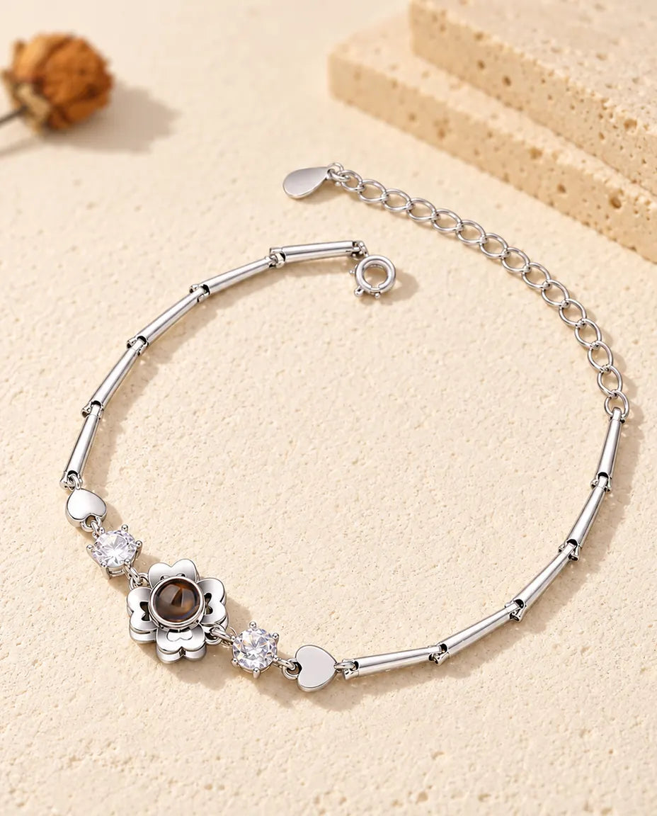 Personligt armband med bild inuti, silverfärgad klöverblomma på smal stavkedja, liggande på krämfärgad gips