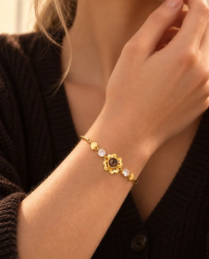 Närbild på det guldfärgade armbandet med klöverblomma och små hjärtlänkar på en handled nära käken