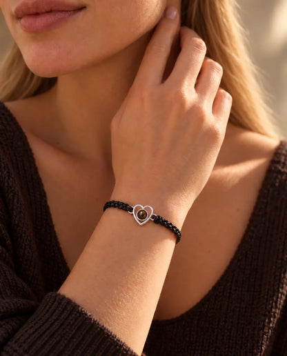 Kvinna med fingertopparna vid sidan av halsen bär armbandet med öppet silverhjärta på svart snodd