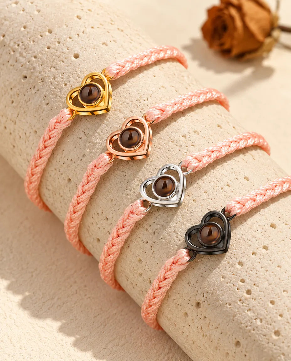Rosa flätade armband med öppet hjärta som visar alla berlockfärger, draperade över travertin