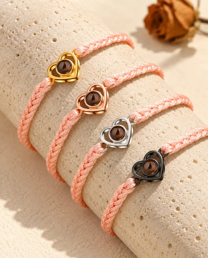 Rosa flätade armband med öppet hjärta som visar alla berlockfärger, draperade över travertin