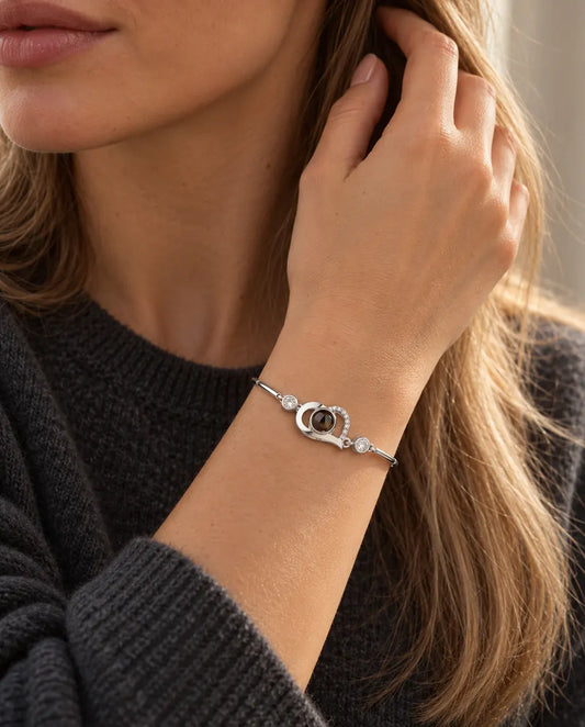 Kvinna med handen i håret som bär det silverfärgade armbandet med öppet hjärta och bild inuti