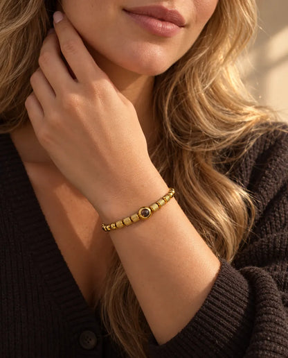 Kvinna som rör vid sidan av halsen och bär det guldfärgade armbandet med räfflade pärlor och bild inuti