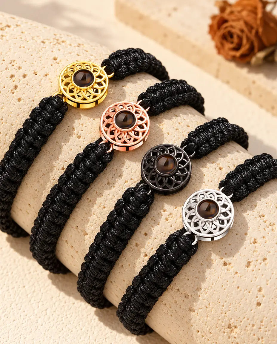 Fyra armband med svart flätad snodd som visar alla berlockfärger, draperade över travertin