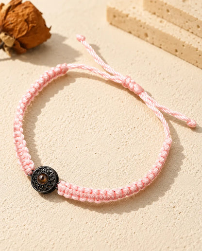 Armband med rosa flätad snodd och svart rund berlock som håller en brun projektionssten