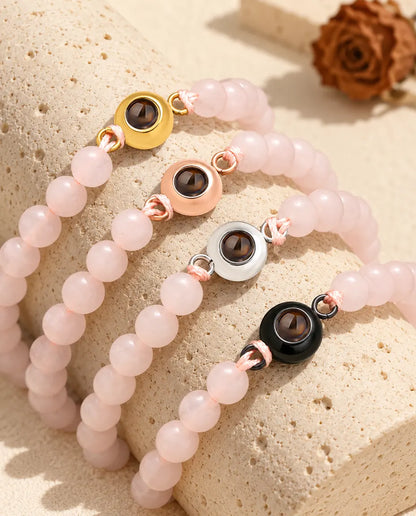 Armband med ljusrosa pärlor och guldfärgade, roséguldfärgade, silverfärgade och svarta ringar sida vid sida