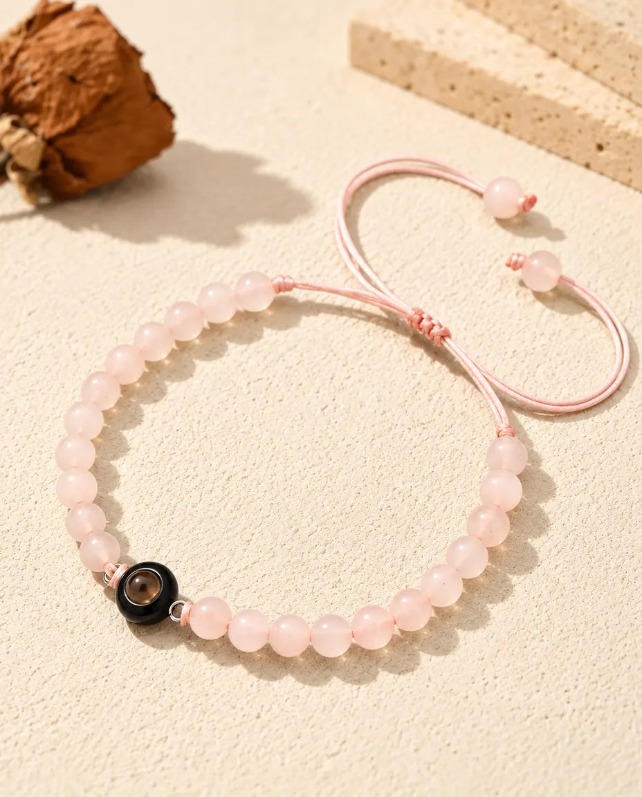 Armband med ljusrosa pärlor och en svart ring med projektionssten på krämvit gips