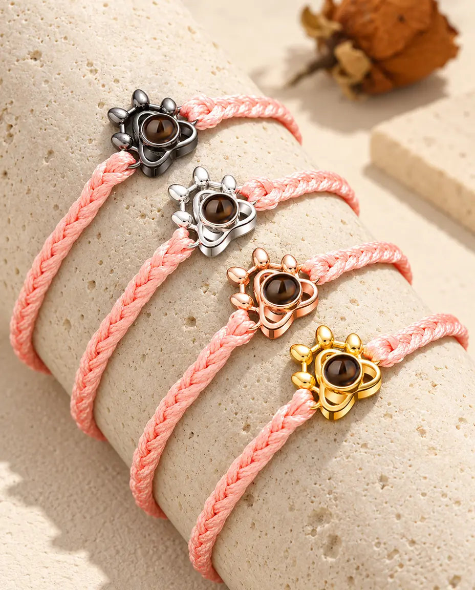 Rosa flätade armband med tassberlock som visar alla berlockfärger, draperade över travertin