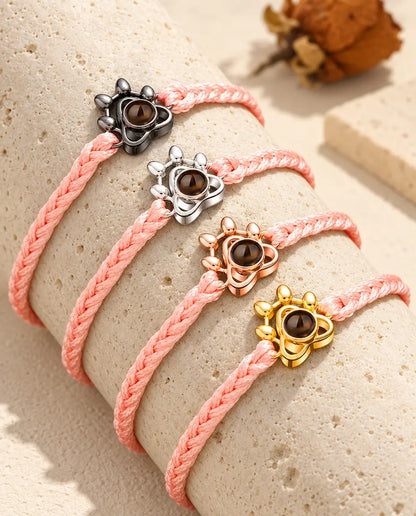 Rosa flätade armband med tassberlock som visar alla berlockfärger, draperade över travertin