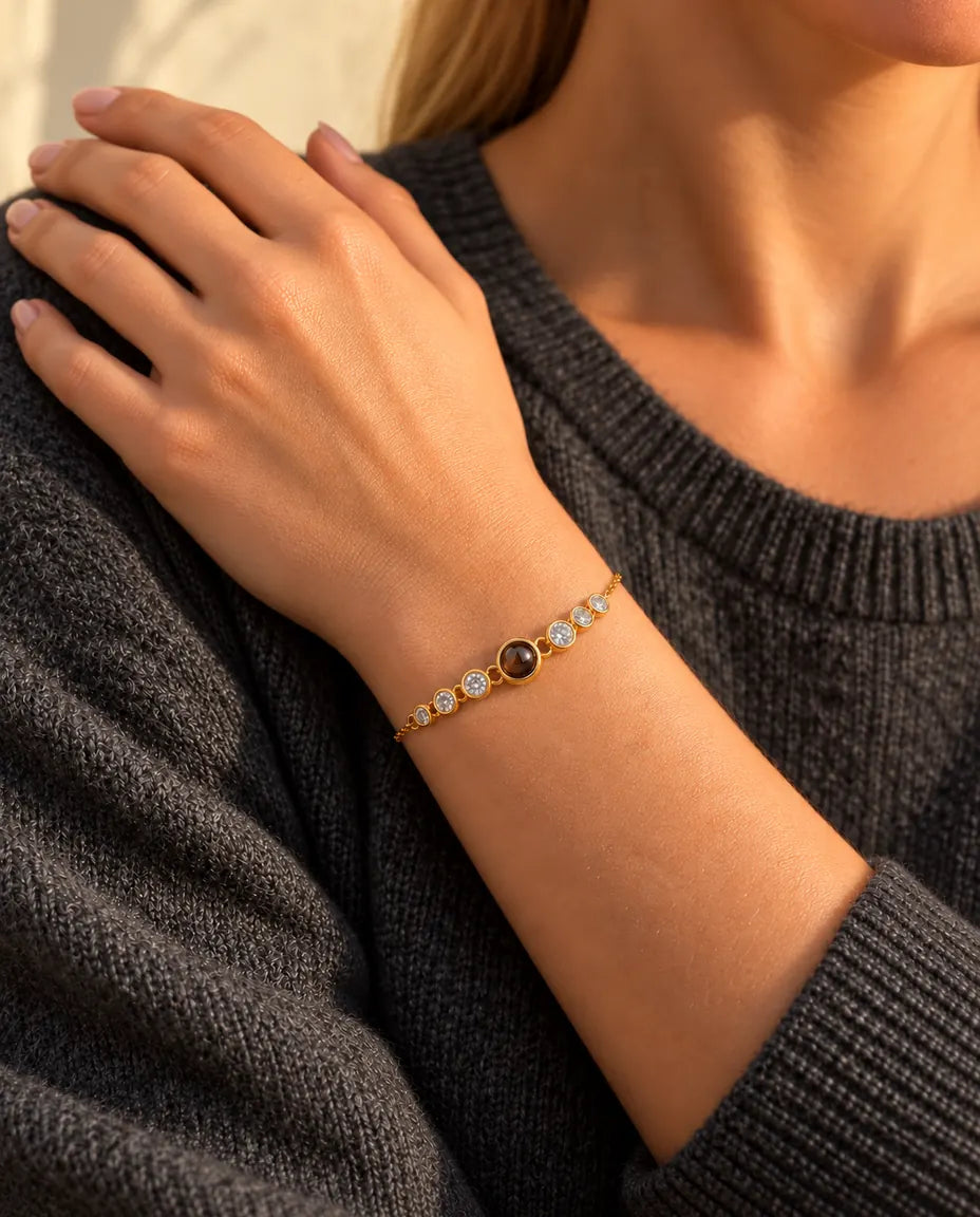 Närbild på det guldfärgade armbandet med zirkonia på en handled, handen vilar mot axeln