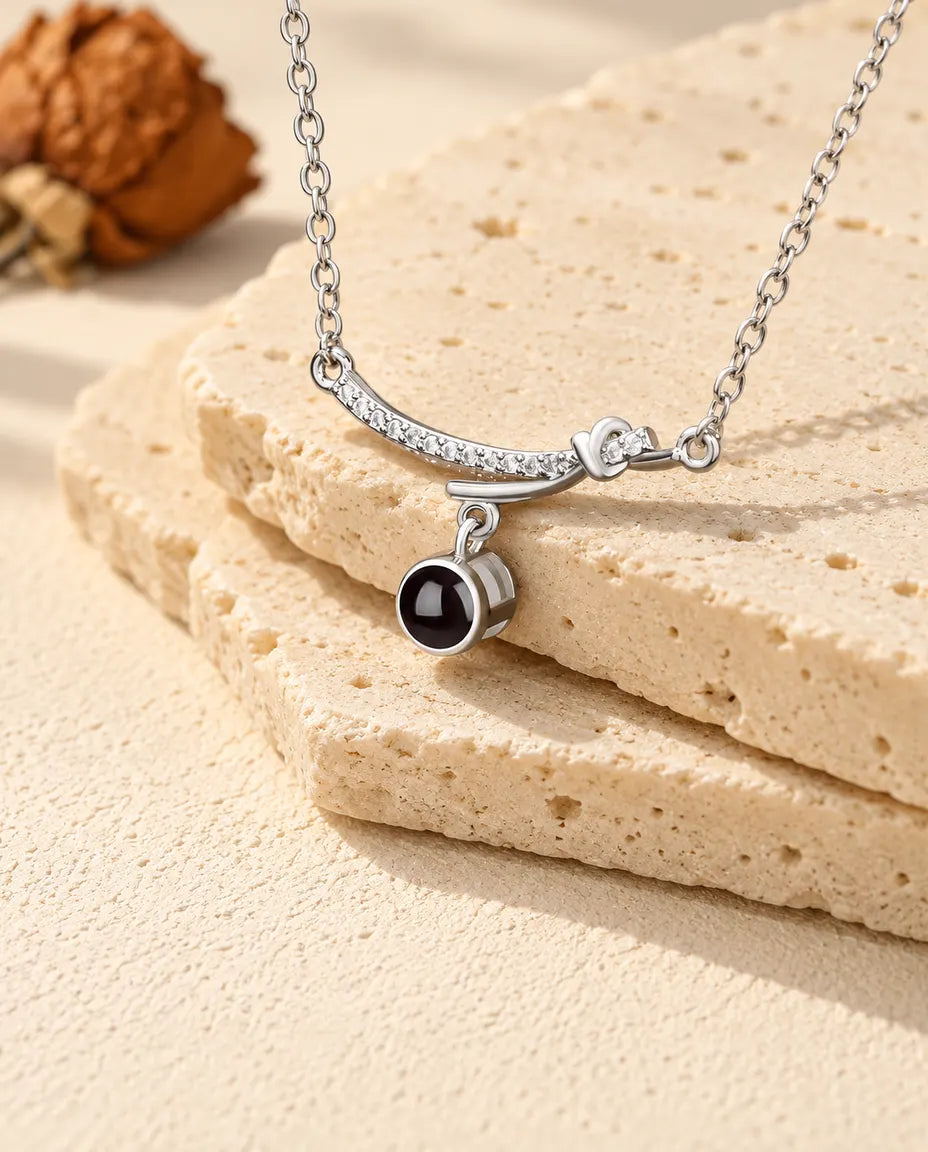 Silverfärgat halsband med böjd stav och bild inuti över kanten på en travertinplatta