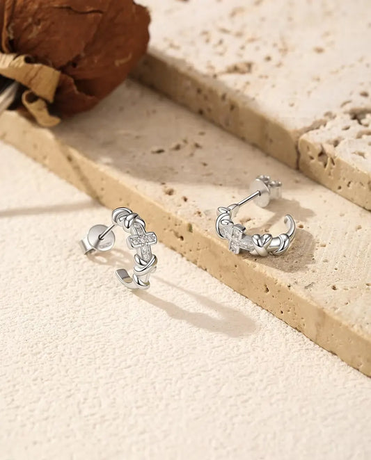 Moissanite Örhängen med Kors i 925 Sterlingsilver - paret bredvid varandra på en ljus strukturerad yta