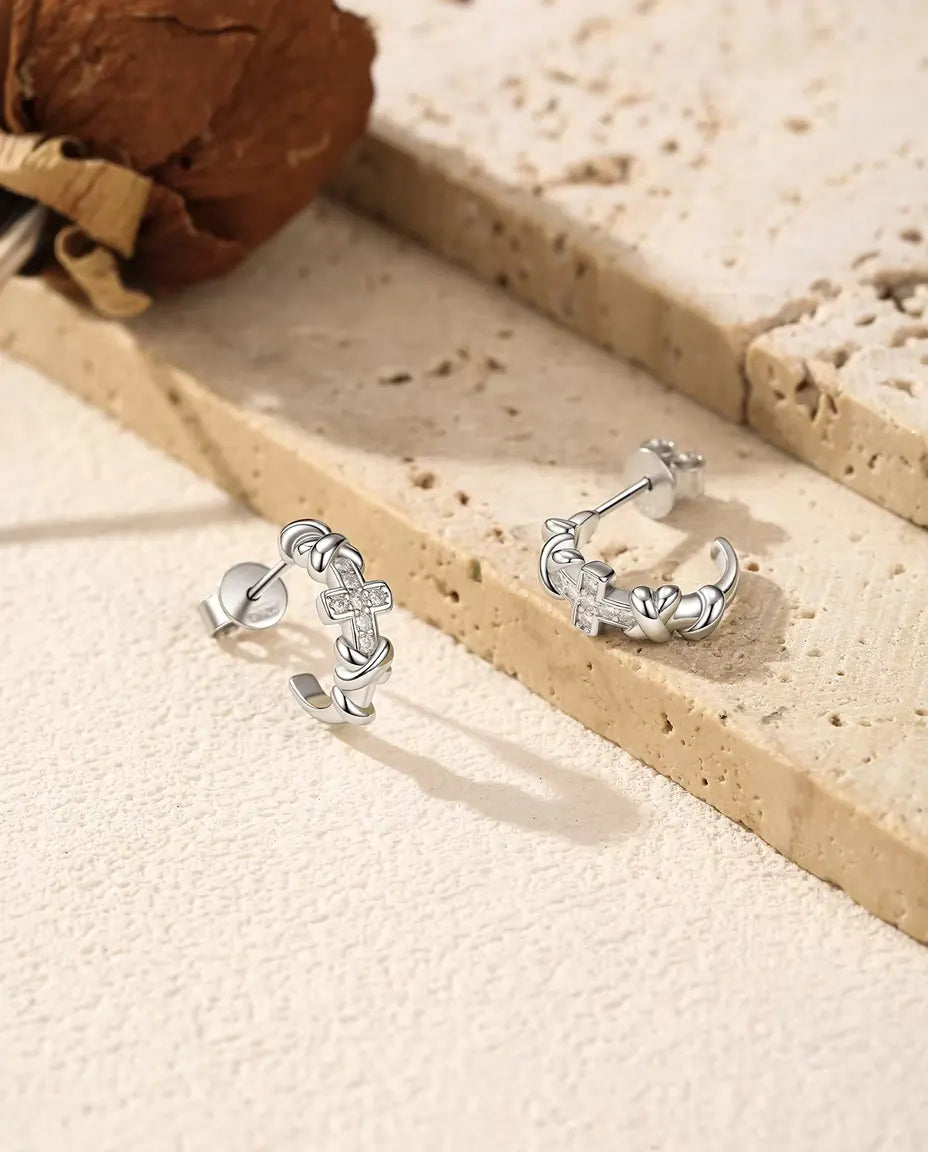 Moissanite Örhängen med Kors i 925 Sterlingsilver - paret bredvid varandra på en ljus strukturerad yta