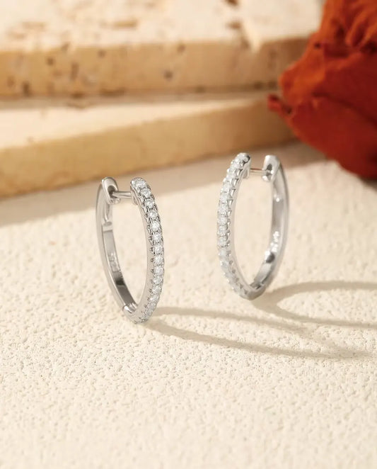Creoler med Moissanite i U-form i 925 Sterlingsilver - paret bredvid varandra på en ljus strukturerad yta