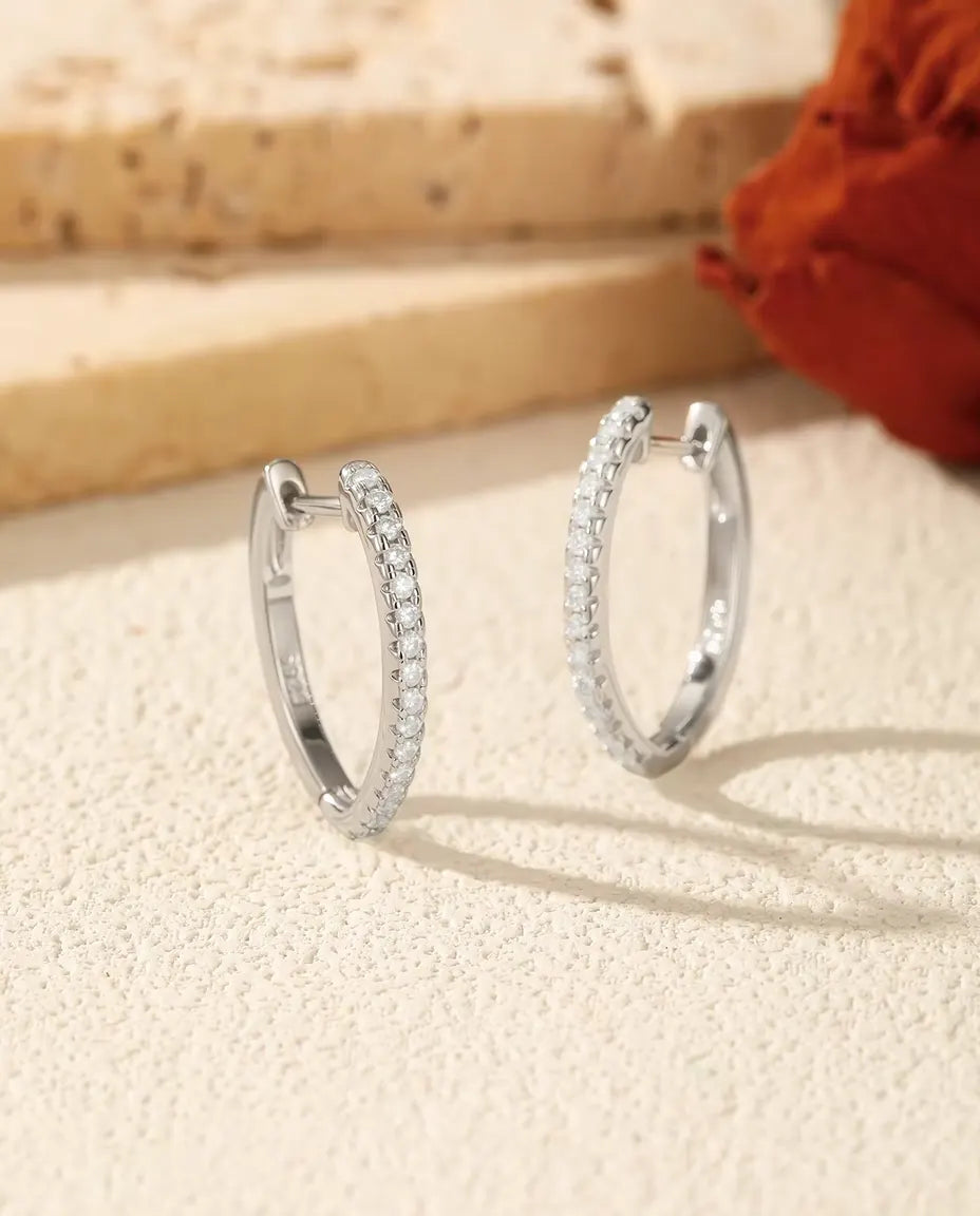 Creoler med Moissanit i U-form i 925 Sterlingsilver - paret bredvid varandra på en ljus strukturerad yta