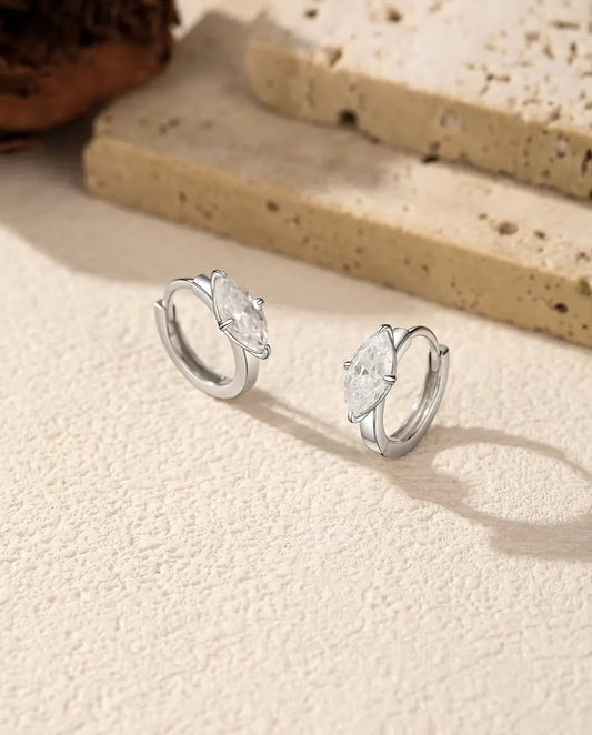 Moissanite Örhängen i 925 Sterlingsilver - paret bredvid varandra på en ljus strukturerad yta
