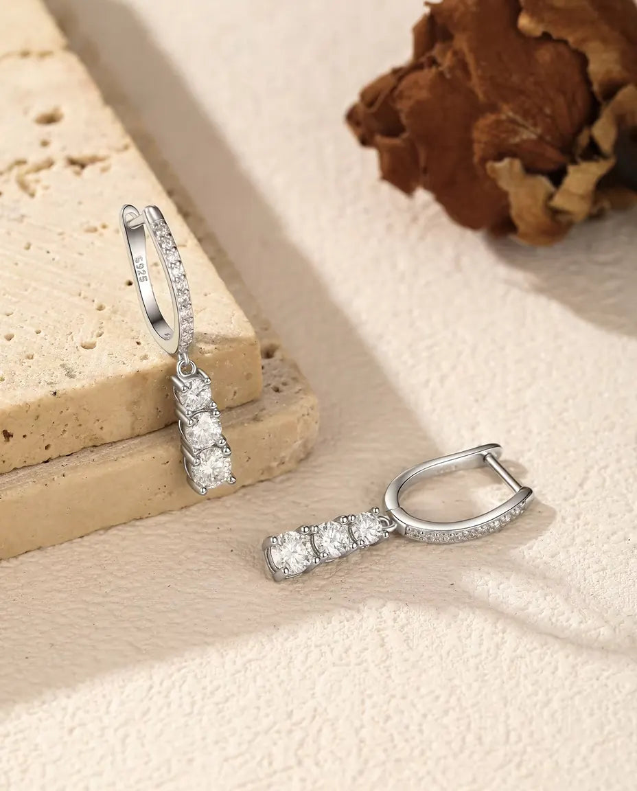 Moissanite Örhängen i 925 Sterlingsilver - ett örhänge hängande från en travertinplatta, det andra liggande bredvid