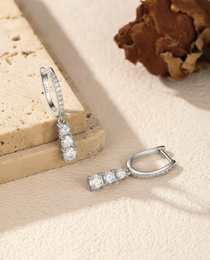 Moissanite Örhängen i 925 Sterlingsilver - ett örhänge hängande från en travertinplatta, det andra liggande bredvid