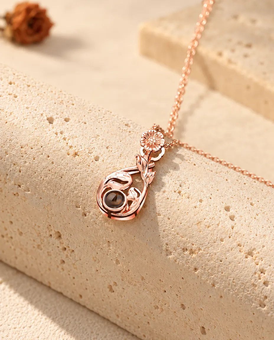 Roséguldfärgat droppformat blomhalsband med bild inuti, hängande över travertin
