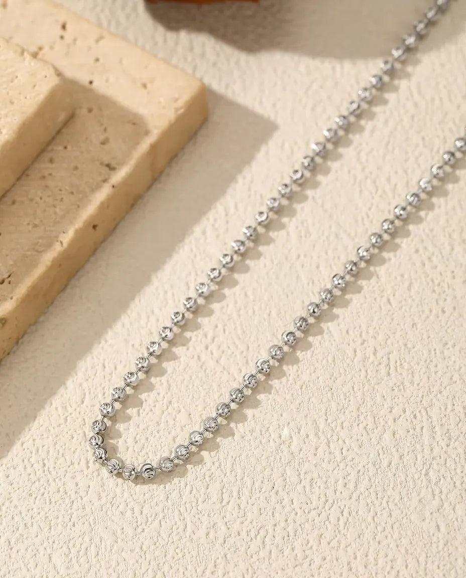Halsband med Fasetterade Kulor i 925 Sterlingsilver - draperat på en ljus yta bredvid en travertinplatta