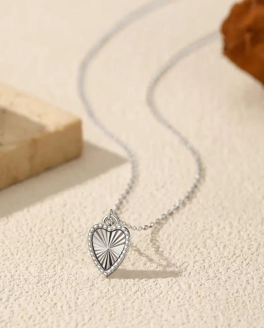 Halsband med Hjärthänge i 925 Sterlingsilver - hänget på en ljus yta bredvid en travertinplatta