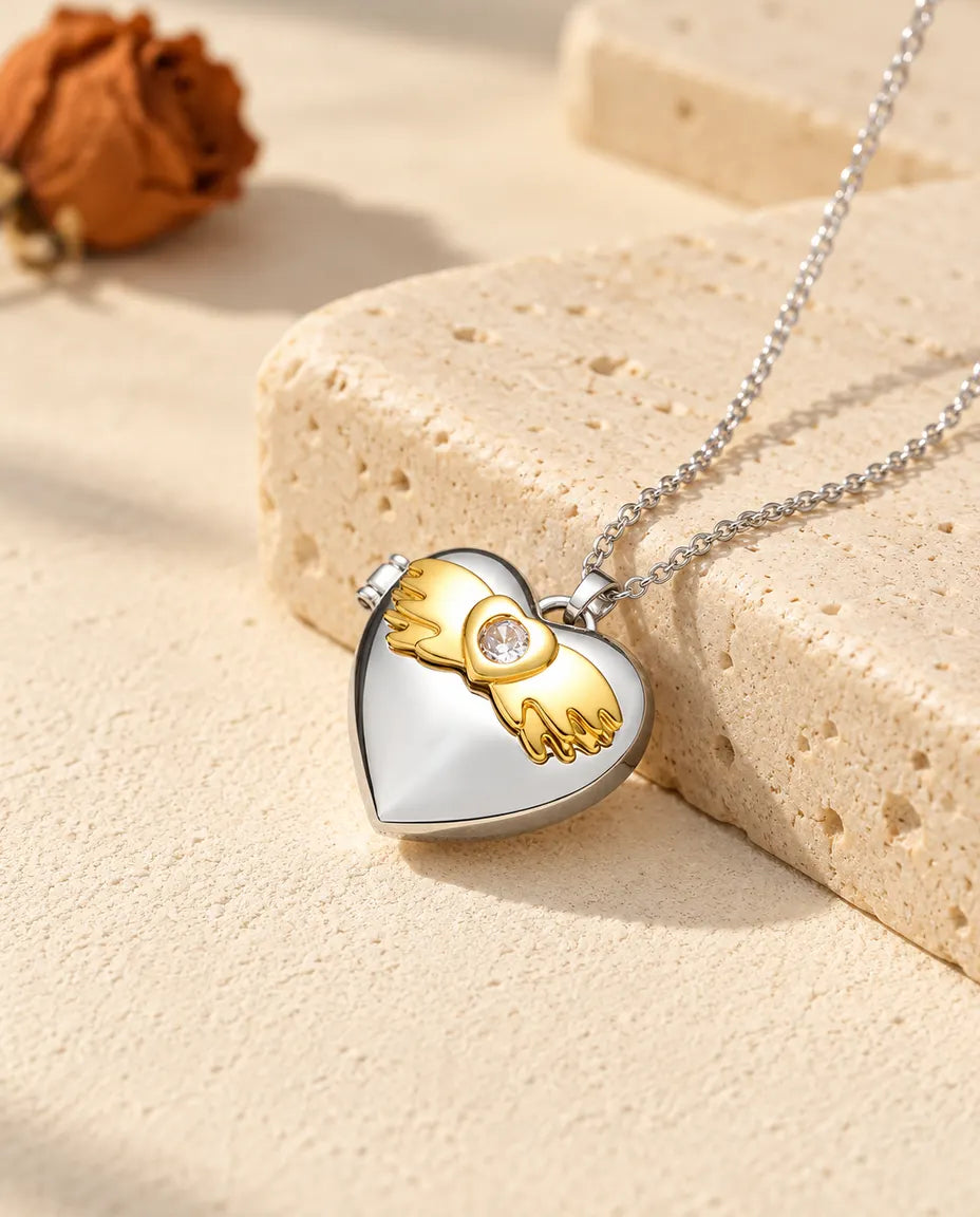 Personlig silverfärgad hjärtmedaljong med guldfärgade änglavingar på locket, lutad mot ett travertinblock
