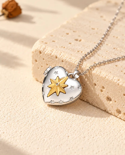 Personlig silverfärgad hjärtmedaljong med en guldfärgad nordstjärna på locket, lutad mot ett travertinblock
