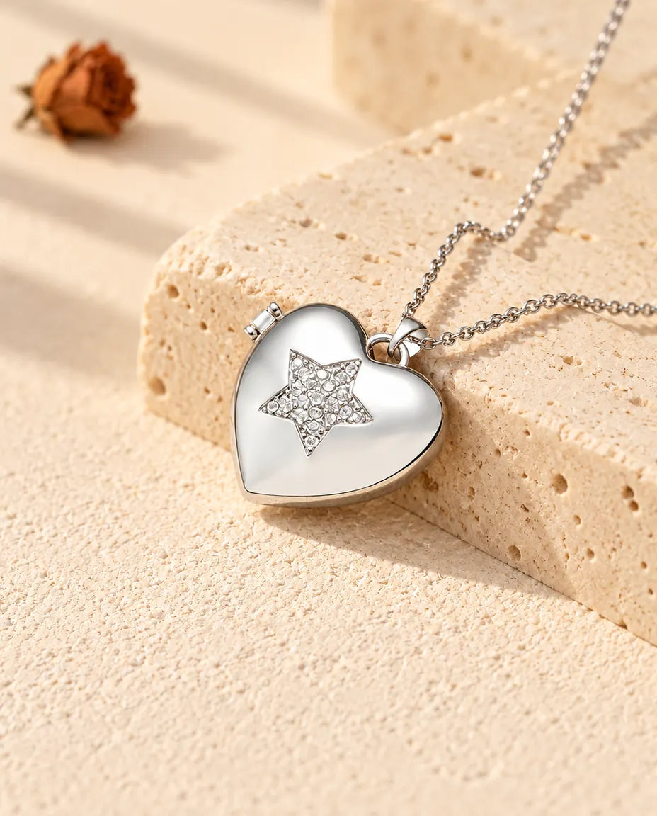Personlig silverfärgad hjärtmedaljong med en stjärna i zirkonia på locket, lutad mot ett travertinblock